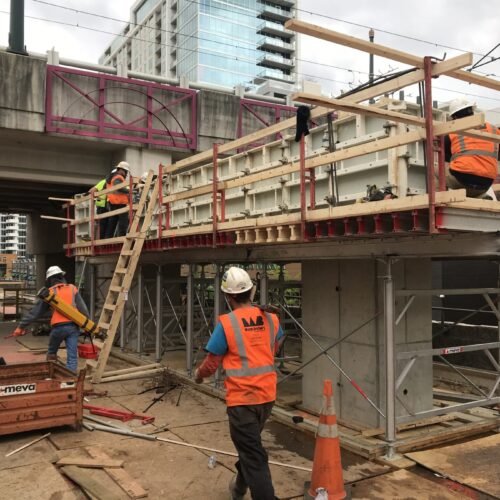 Workers in safety gear build concrete formwork under an overpass.