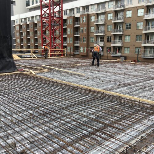Construction workers prep rebar on building floor near apartments.