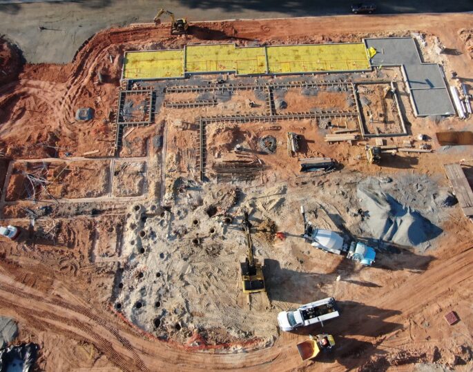Aerial view of construction site with vehicles, workers, foundations.