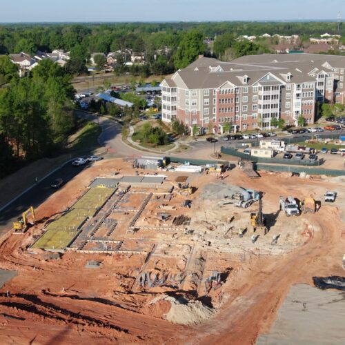 Aerial view: construction site foundations, equipment, next to apartments.