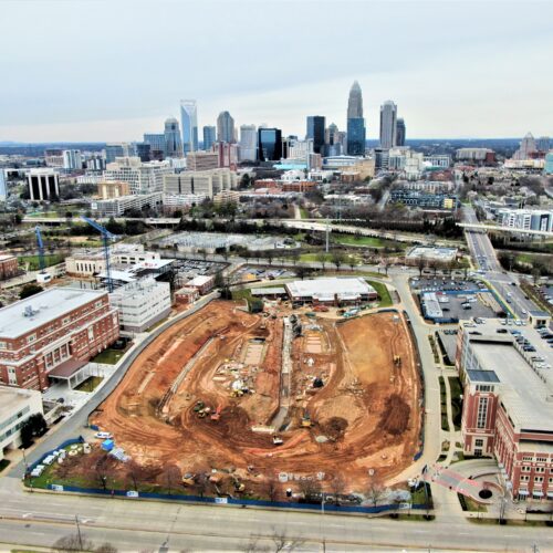 Construction site in front of city buildings under gray sky.
