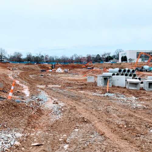 Construction site with dirt roads, pipes, equipment, and buildings.