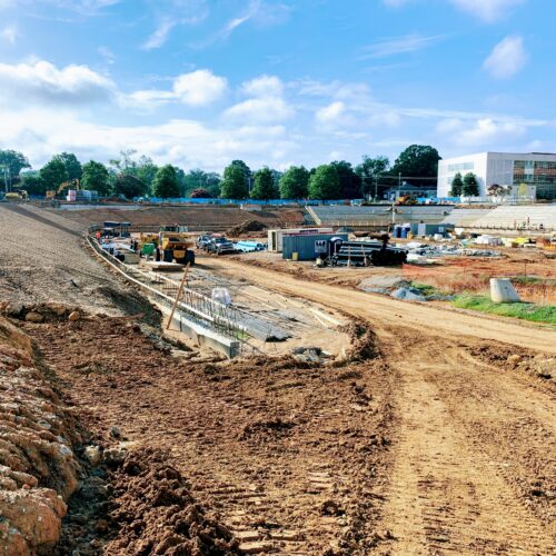 Construction site with machinery, materials, dirt paths, cloudy sky.