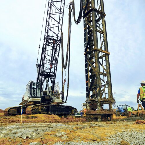 Construction worker by drilling equipment under clear sky.