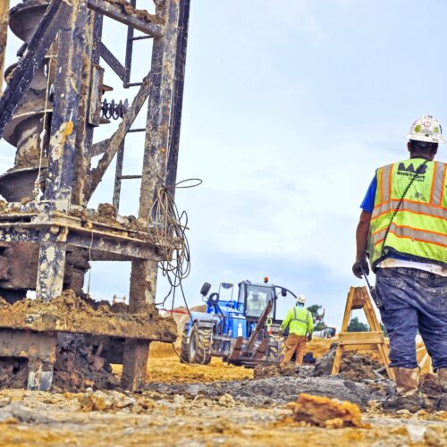 Worker in safety vest stands by heavy equipment on muddy site.