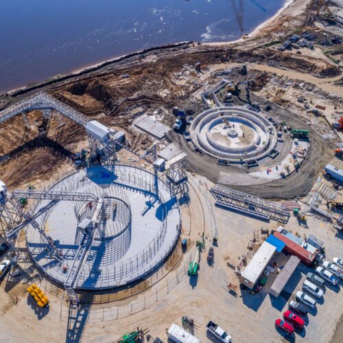 Aerial view: circular construction site, vehicles, equipment, river nearby.