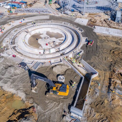 Aerial view: workers and machines build large concrete circle.