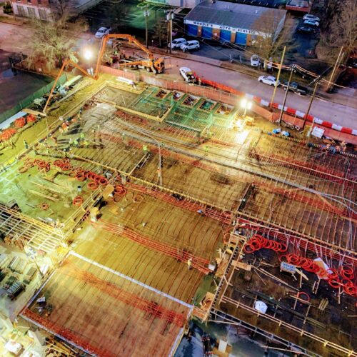 Night aerial view of lit construction site with workers and machinery.