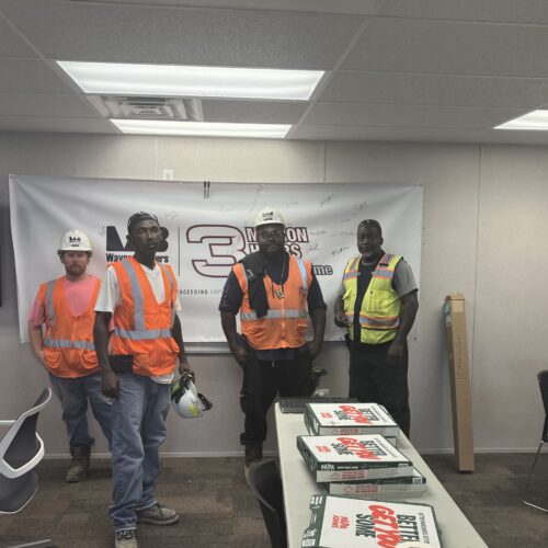 Four workers in safety gear stand by pizza boxes in office.