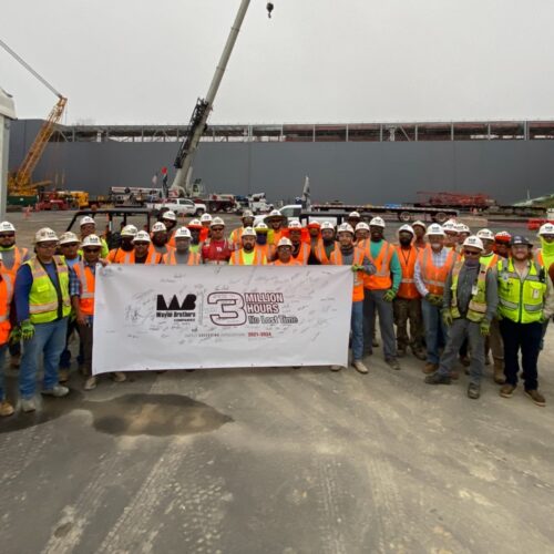 Construction workers in safety gear hold Three Million Safe Hours banner.