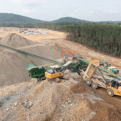 Construction vehicles work on gravel mound at quarry site.