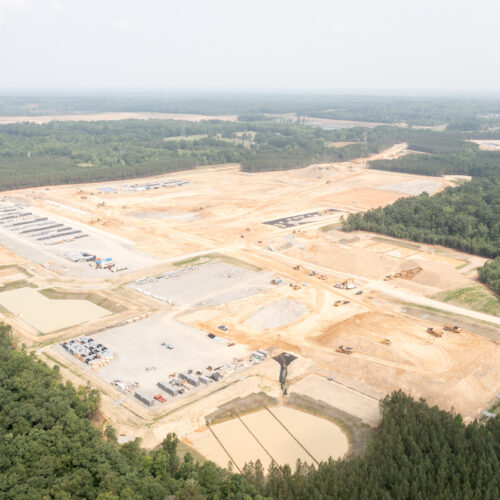 Aerial view of construction site, vehicles, materials, and trees.