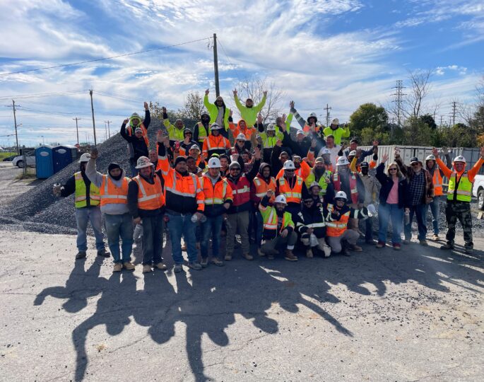 Construction workers in safety gear pose together outdoors, celebrating.