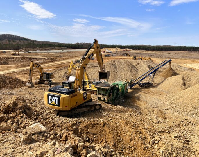 Excavators move dirt and gravel at a sunny construction site.