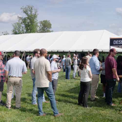 People gather on grass near white tents and a canopy.