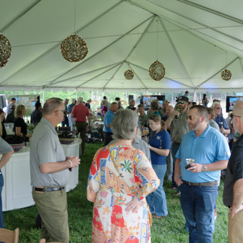 People mingling with drinks under a white outdoor event tent.