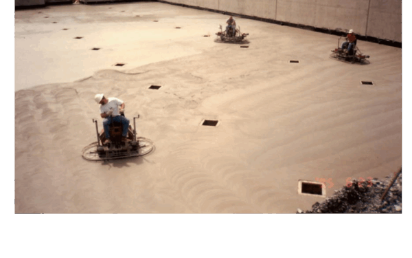 Three workers operating ride-on trowels on a concrete pad