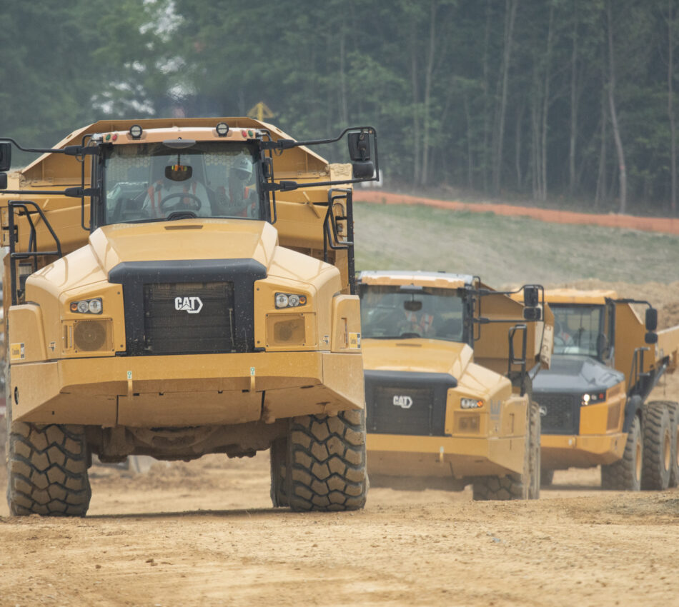 Three yellow Caterpillar dump trucks drive in a line