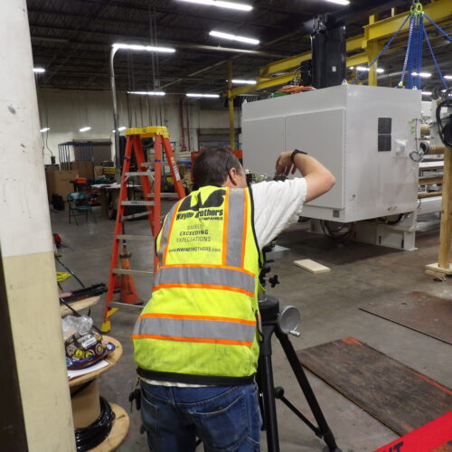 Man in safety vest sets up camera in industrial warehouse.