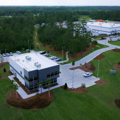 Aerial view of two office buildings amid greenery and roads.