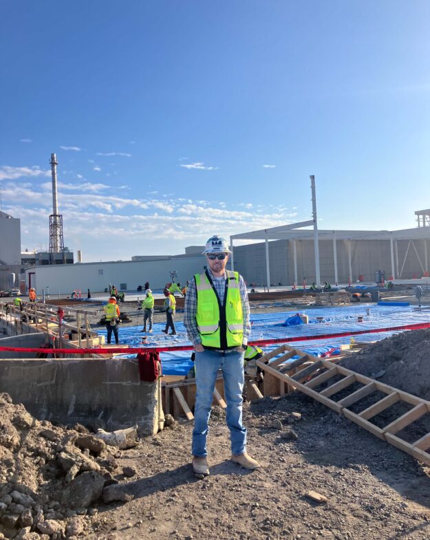 Person in safety gear at construction site with workers behind.