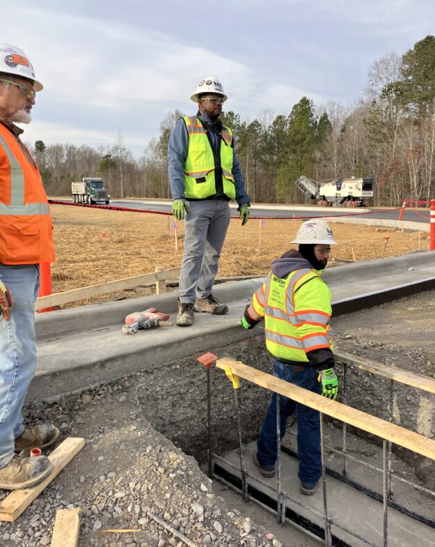 Three workers in safety gear stand by a concrete structure.