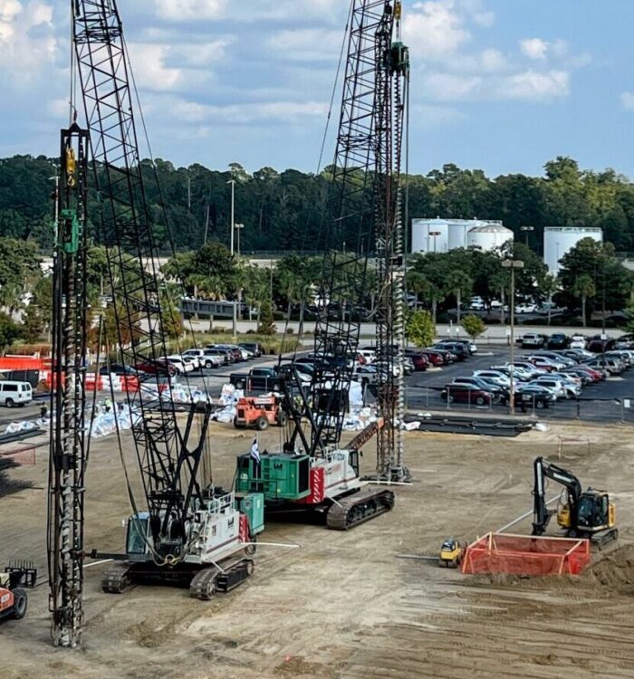 Construction vehicles at worksite; plane near runway in background.