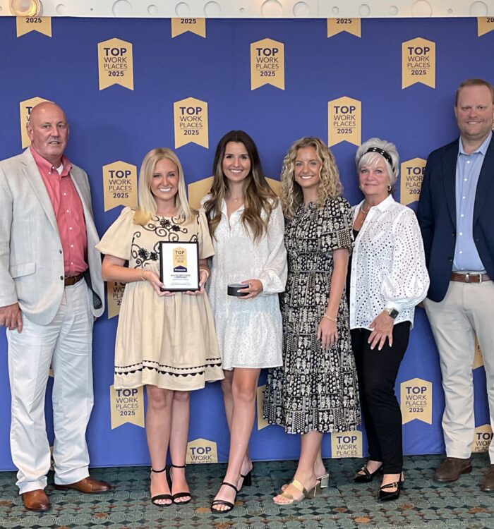 Six people pose by a Top Workplaces 2023 backdrop, holding awards.