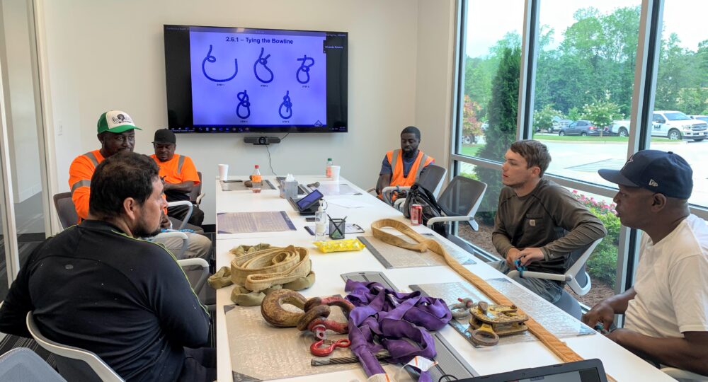 Group of men sitting around a boardroom table with a knot-tying presentation displayed on screen