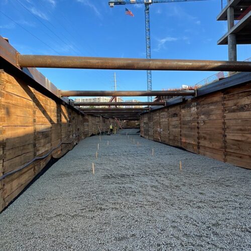 Construction site: deep trench, wood walls, gravel, workers, crane.