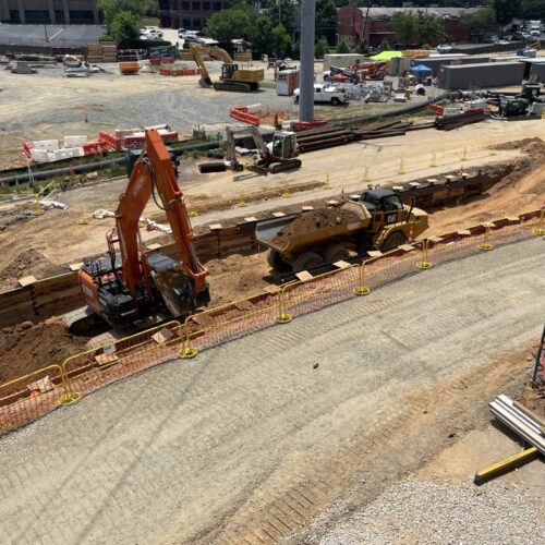 Excavator and dump truck working in a sunny, barriered trench.