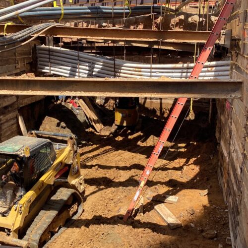 Construction site: machines, wooden walls, overhead pipes, red ladder.