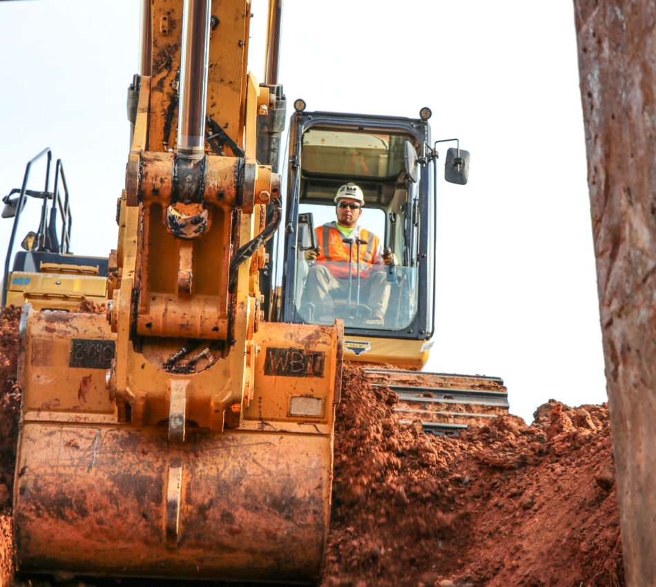 A construction worker scoops up dirt using an excavator
