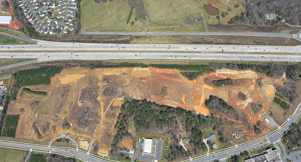 Aerial view of large construction site near highway and homes.