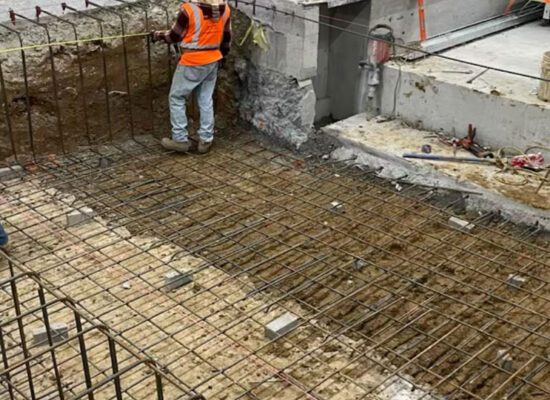 Two workers in safety gear inspect rebar at building site.