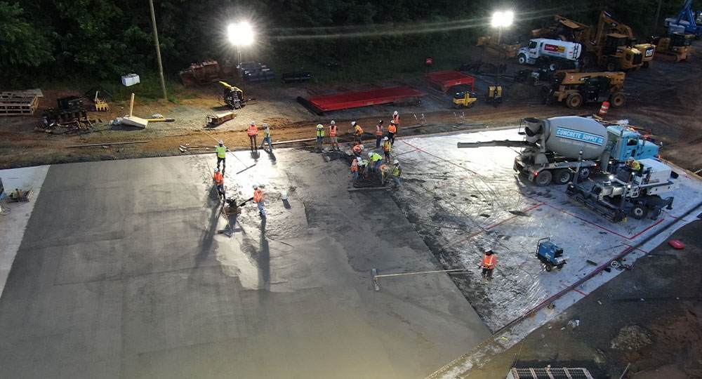 Workers in safety gear smooth concrete slab at night.