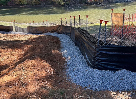 Riverside construction with silt fence, orange barriers, gravel, exposed soil.