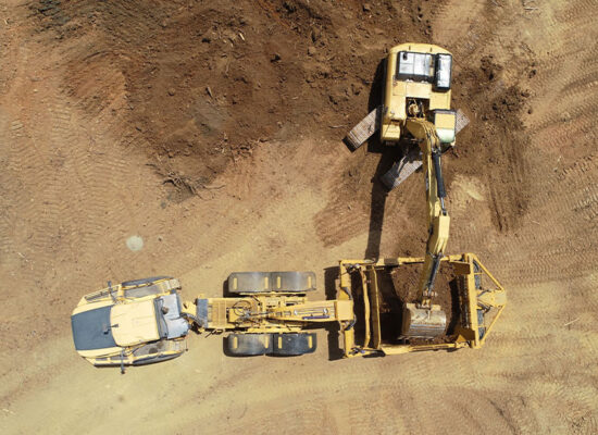Excavator loads soil into dump truck; tire tracks visible.