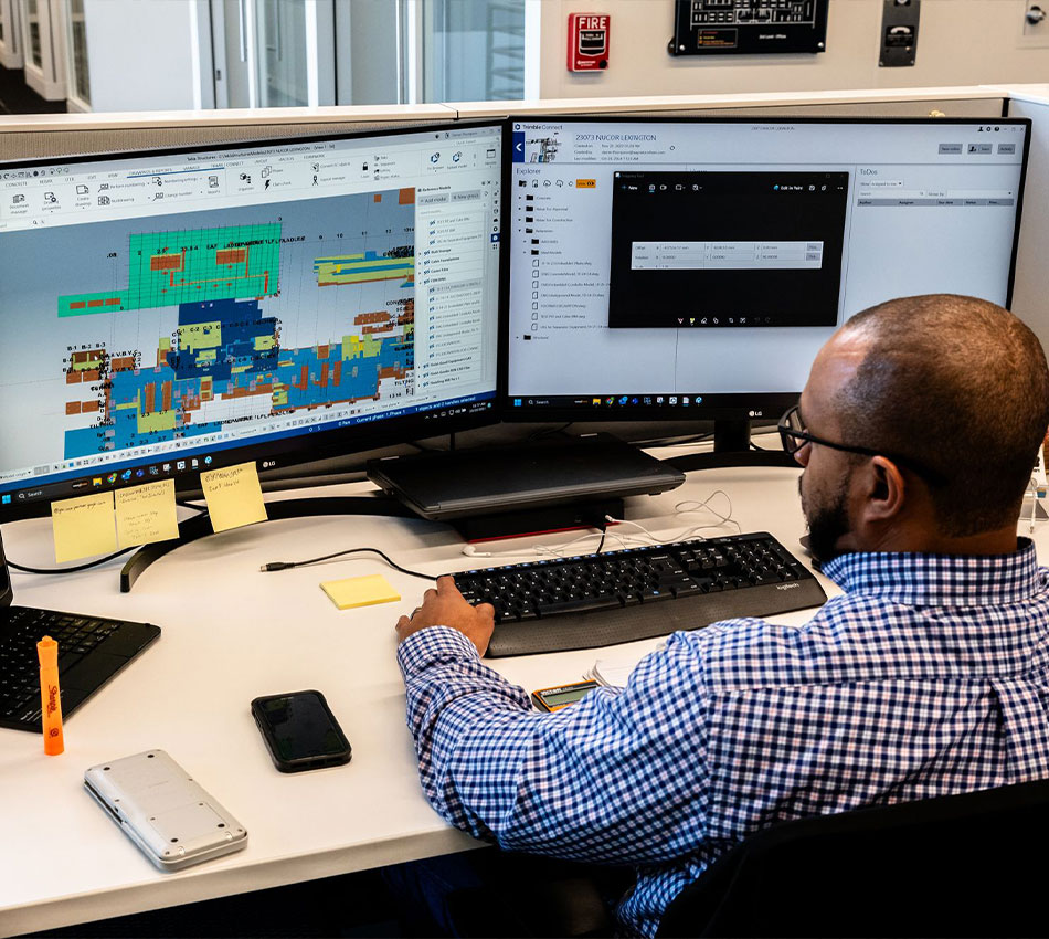 Man works at desk with two monitors, 3D rendering on screen
