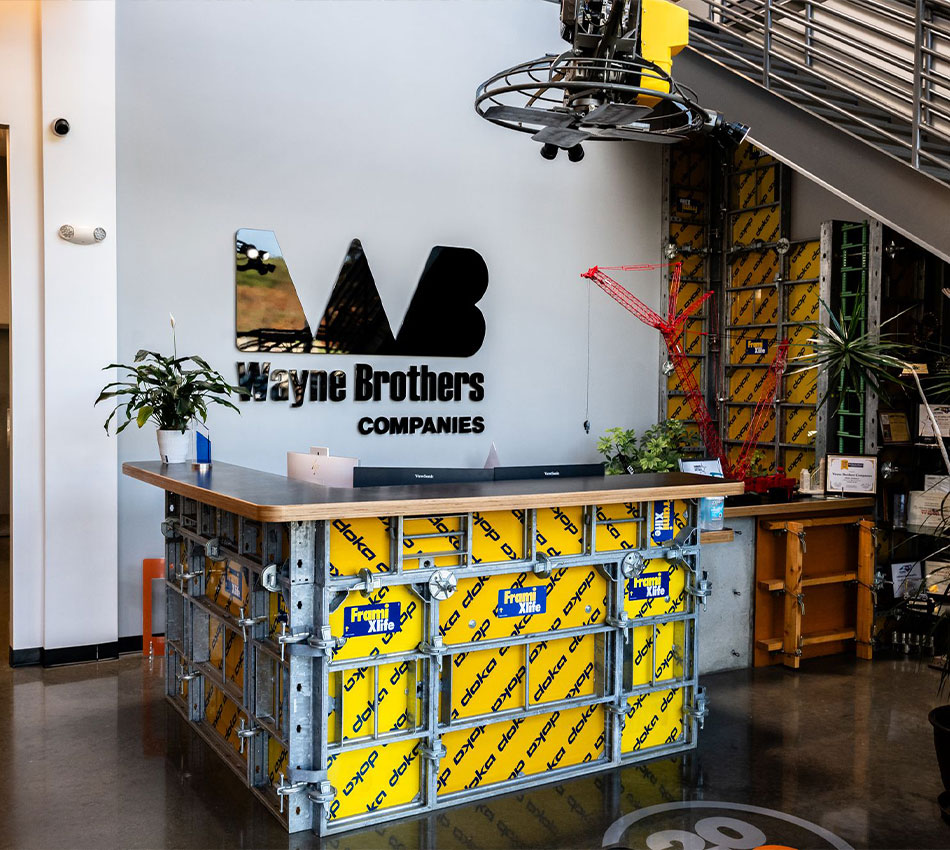 Reception desk made of construction materials before Wayne Brothers sign.