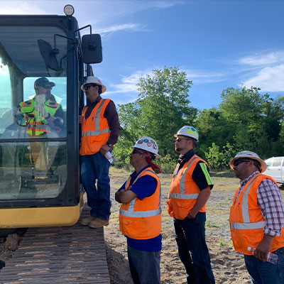 Five construction workers stand by a large vehicle outdoors.