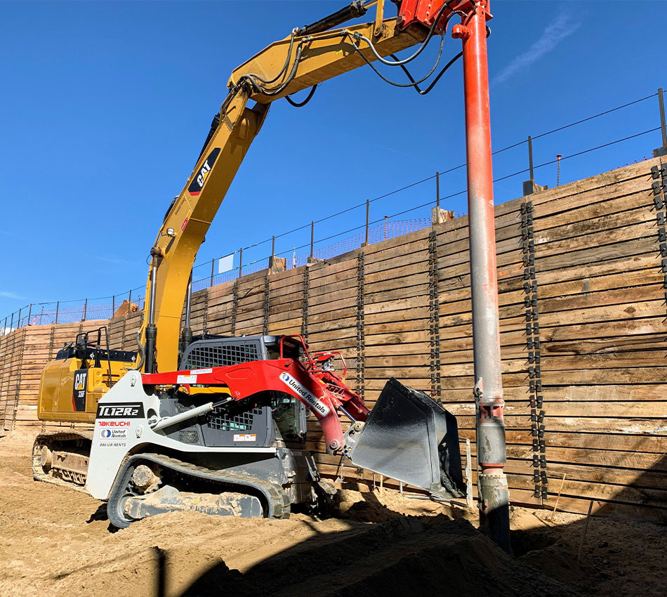 Skid steer and excavator install steel pipe at construction site.