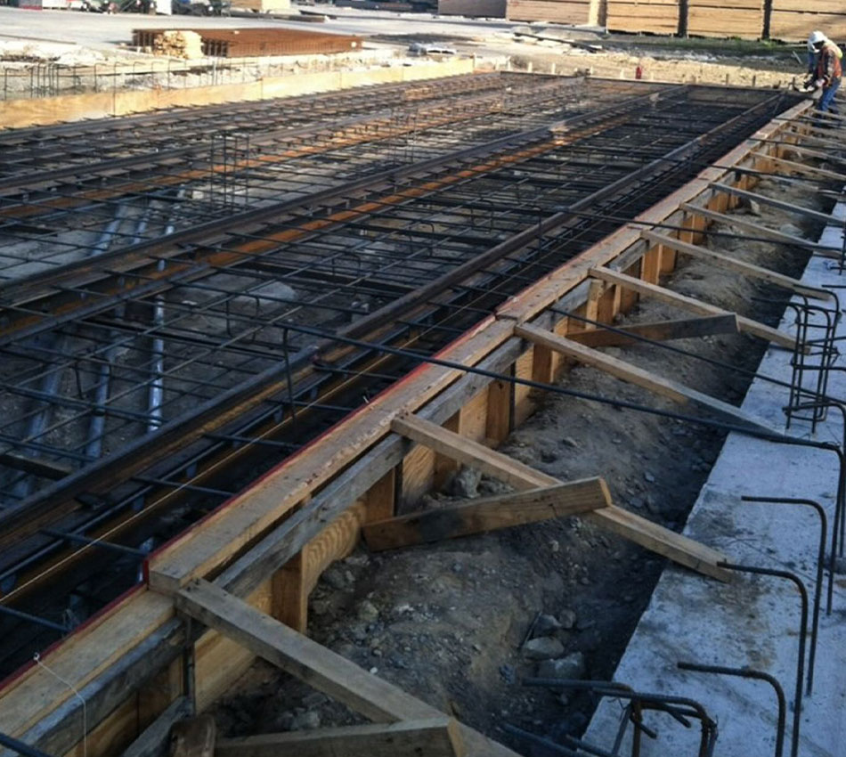 Construction site with concrete foundation, exposed rebar, and formwork.