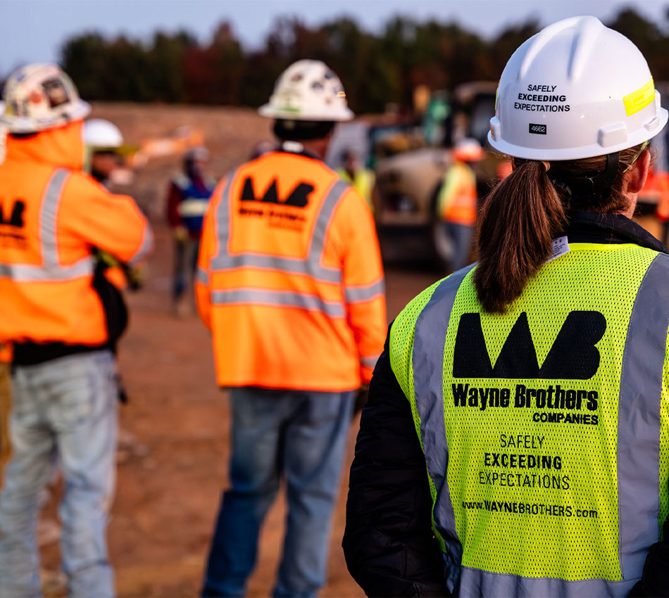 Construction workers in Wayne Brothers safety vests stand outside.