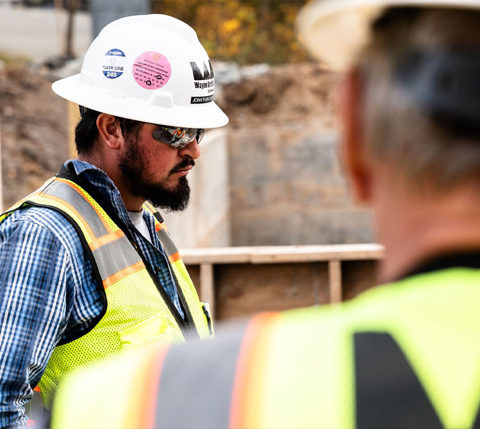 Two workers in hard hats and vests at construction site.