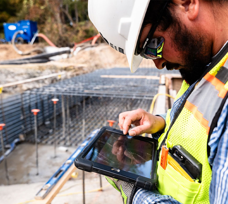 Construction worker with helmet uses tablet at building site.