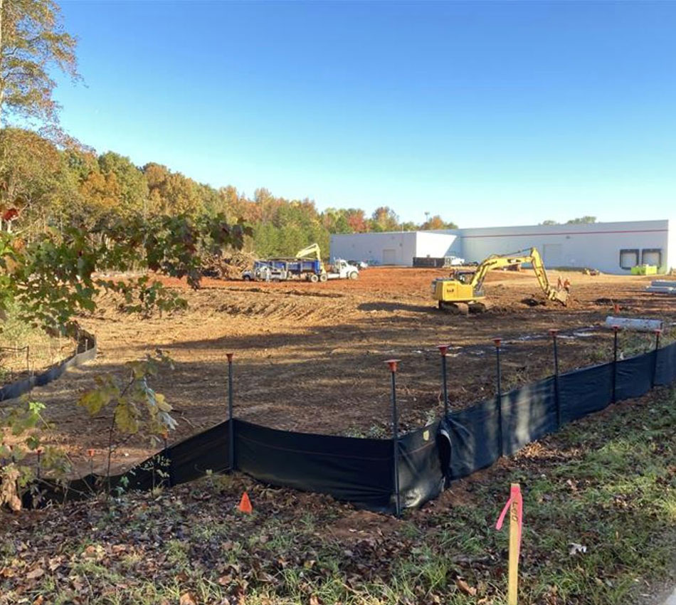 Excavators work on cleared site near industrial building, trees.