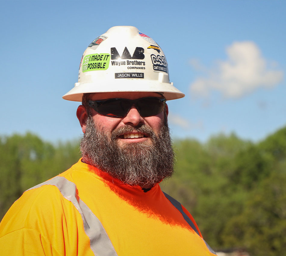 Man in orange safety shirt and hard hat smiles at the camera.