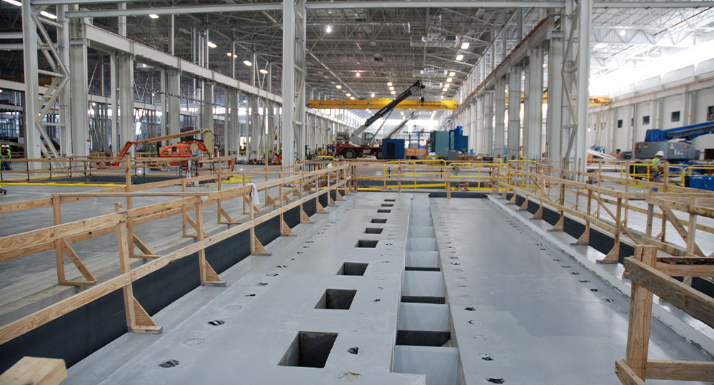 Industrial warehouse with cranes, equipment, and fenced concrete pit.