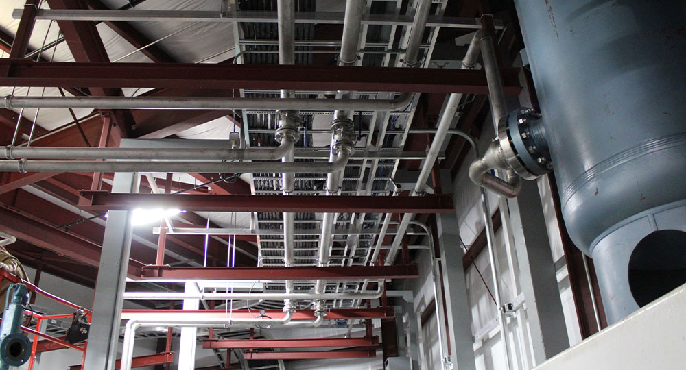 Industrial interior with exposed pipes, metal beams, and large tank.